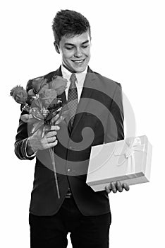 Young happy businessman smiling while holding red roses and looking at gift box ready for Valentine`s day