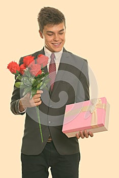 Young happy businessman smiling while holding red roses and looking at gift box ready for Valentine's day