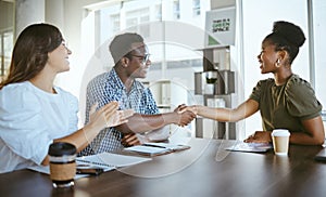 Young happy businesspeople shaking hands in a meeting with a colleague clapping at work. Cheerful hispanic businesswoman