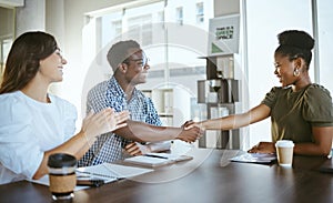 Young happy businesspeople shaking hands in a meeting with a colleague clapping at work. Cheerful hispanic businesswoman