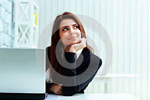 Young happy businesswoman sitting on her workplace and looking at copyspace