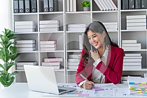 Young happy businesswoman talking on cellphone make notes and using laptop computer working online in modern office.