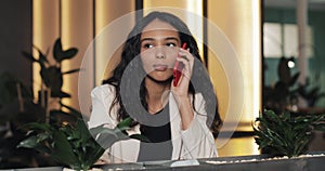 Young happy businesswoman talking on the phone while sitting in cafe. She is smiling and drinking coffee. Beautiful girl