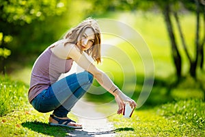 Young happy Caucasian blonde woman with coffee beverage sitting in park