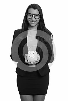 Young happy Caucasian businesswoman smiling and holding piggy bank