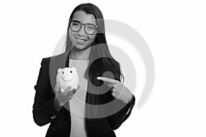 Young happy Caucasian businesswoman smiling and holding piggy bank while pointing finger