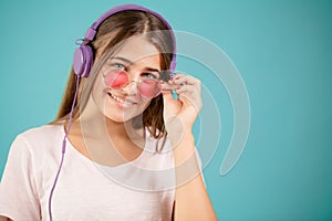 Young happy Caucasian femal is wearing blue headphones and pink sunglasses