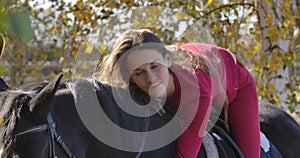 Young happy Caucasian female equestrian lying on horseback and caressing her pet. Beautiful black horse standing in the