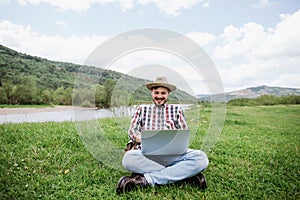 Young happy caucasian man freelancer working on his laptop outdoors in the mountains