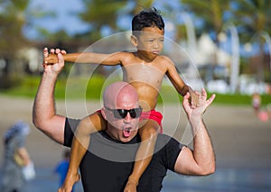 Young happy Caucasian man and his mixed Asian ethnicity young son at tropical beach Summer holidays the child sitting on his