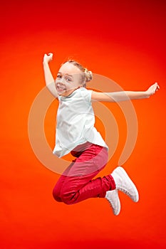 Young happy caucasian teen girl jumping in the air, isolated on red studio background.