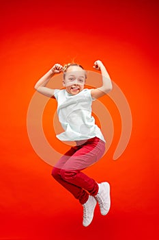 Young happy caucasian teen girl jumping in the air, isolated on red studio background.