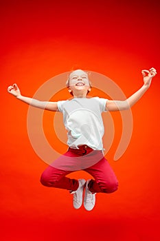 Young happy caucasian teen girl jumping in the air, isolated on red studio background.