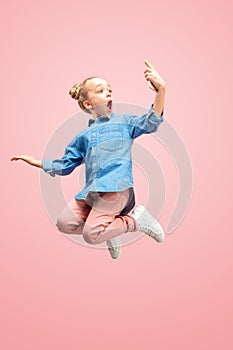 Young happy caucasian teen girl jumping with phone in the air, isolated on pink studio background.