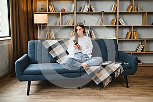 Young happy caucasian woman she 20s in casual clothes hold in hand use mobile cell phone sit on blue sofa indoor rest at