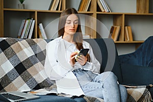 Young happy caucasian woman she 20s in casual clothes hold in hand use mobile cell phone sit on blue sofa indoor rest at