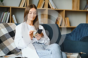 Young happy caucasian woman she 20s in casual clothes hold in hand use mobile cell phone sit on blue sofa indoor rest at