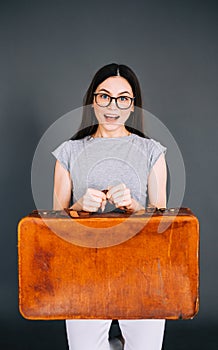 Young happy caucasian woman holding travel baggage isolated on gray background. Ready for traveling