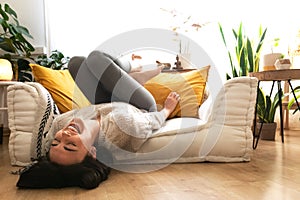 Young happy caucasian woman laughing out loud lying upside down on the sofa. Copy space.