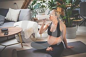 Young happy and cheerful beautiful pregnant woman taking a break, hydrating, drinking water from the botle after home