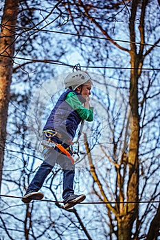 Young happy child boy in adventure park in safety equipment.