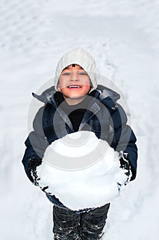 Young happy child playing with a big snow ball