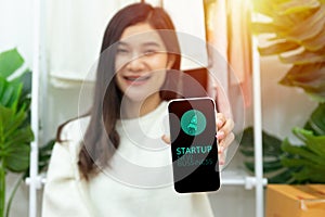 Young happy confident small business owner Asian woman showing smartphone with screen display for startup new business with rocket
