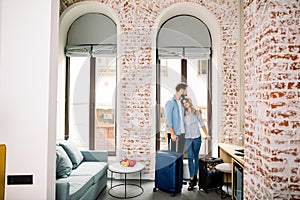 Young happy couple arrived to hotel room on honeymoon or business trip. Handsome man and charming woman in casual wear