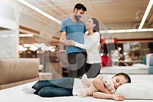 Young happy couple in background enjoying sleeping little girl. Choosing mattress in store.