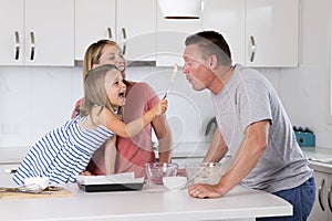 Young happy couple baking together with little young beautiful daughter at home kitchen having fun playing with cream in family li