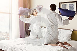 Young happy couple in bathrobe fight pillows on bed photo