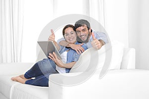 Young happy couple on couch at home enjoying using digital tablet computer