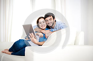 Young happy couple on couch at home enjoying using digital tablet computer