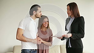 Young happy couple discussing contract and shaking hands with contractor