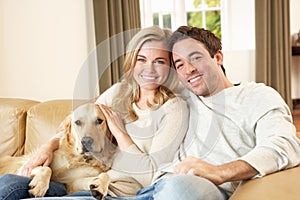 Young happy couple with dog sitting on sofa