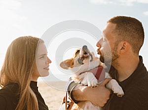 Young happy couple with dog walking on beach. Beautiful girl and guy and Corgi puppy