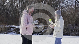 Young happy couple drinks a hot tea and eats snacks after rides ice skating on frozen lake in forest