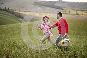 A young happy couple enjoying the nature and a large meadow while looking for a picnic spot. Love, relationship, together, nature