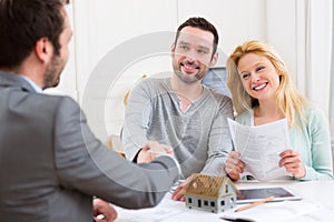 Young happy couple handshaking real estate agent after signing c