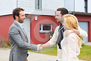 Young happy couple handshaking real estate agent after signing contract