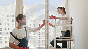 Young happy couple is having fun while doing cleaning at home. A team of workers cleans the white windows of an office