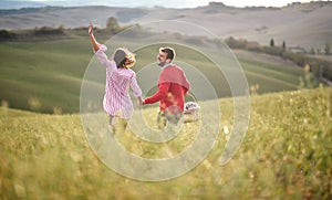 A young happy couple having fun while walking over a large meadow looking for a picnic spot. Love, relationship, together, nature