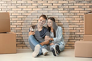 Young happy couple with house model and moving boxes sitting on floor at new home