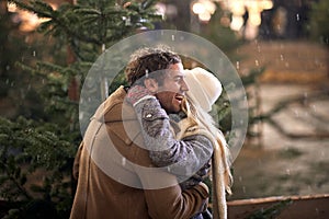 A young happy couple in a hug on a snowy weather in the city. Christmas tree, love, relationship, Xmas, snow