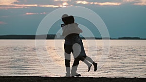 Young happy couple hugging on sunset on the beach. Attractive man and woman whirling on the shore of river in evening.
