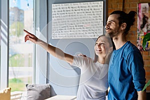 Young happy couple hugging together looking out the window