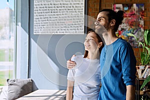 Young happy couple hugging together looking out the window