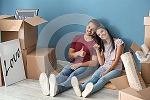 Young happy couple with key and moving boxes sitting on floor at new home