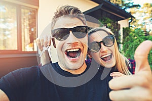 Young happy couple with keys in hand standing outside of their new home