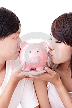 Young happy couple kiss pink piggy bank